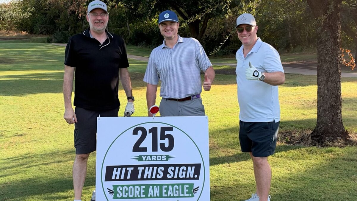Golfers at the PPAS tournament beside PromoEQP's hole sign: 215 yards, hit this sign, score an eagle